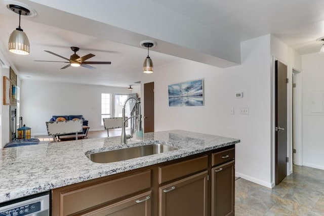 kitchen featuring dishwasher, light stone counters, a sink, and decorative light fixtures