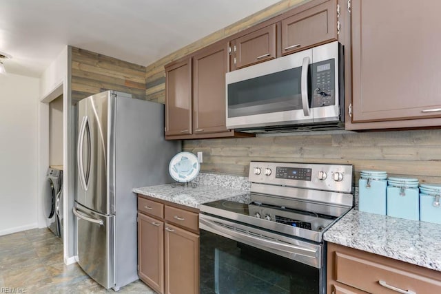 kitchen with baseboards, light stone countertops, stainless steel appliances, separate washer and dryer, and backsplash