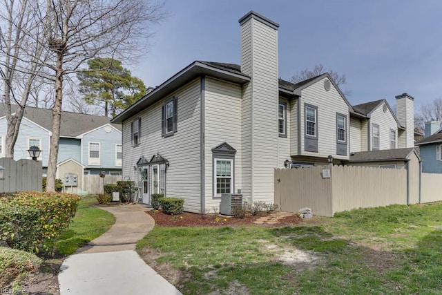 view of property exterior featuring a yard, a chimney, cooling unit, and fence