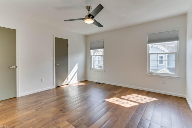 spare room with a ceiling fan, visible vents, baseboards, and wood finished floors