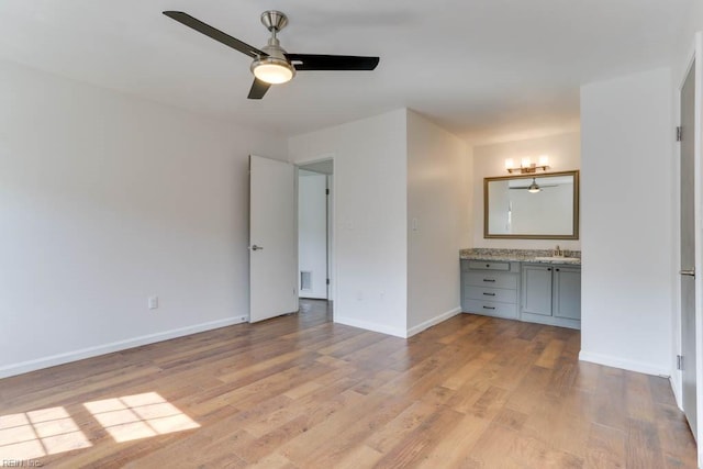 unfurnished bedroom featuring light wood finished floors, a ceiling fan, a sink, ensuite bath, and baseboards