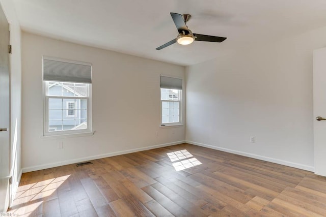 unfurnished room with a ceiling fan, visible vents, baseboards, and wood finished floors