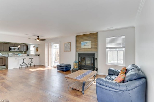 living area with ceiling fan, a fireplace, visible vents, baseboards, and light wood-type flooring