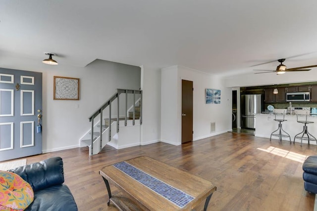 living area with a ceiling fan, stairs, visible vents, and wood finished floors