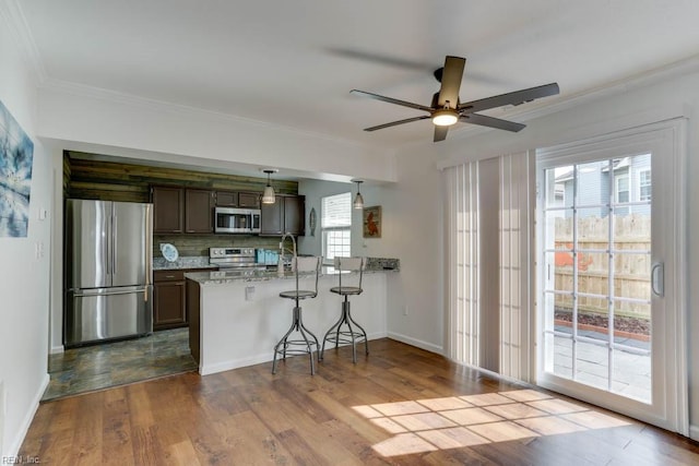 kitchen featuring stainless steel appliances, a peninsula, a kitchen breakfast bar, backsplash, and dark wood finished floors