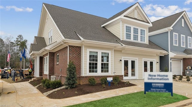 view of front facade featuring a garage, french doors, brick siding, and roof with shingles