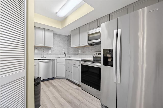 kitchen with decorative backsplash, appliances with stainless steel finishes, light countertops, gray cabinetry, and light wood-style floors