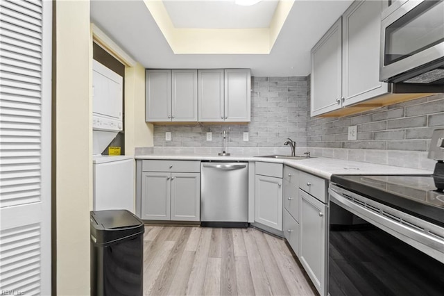 kitchen featuring stacked washer / dryer, a sink, light countertops, appliances with stainless steel finishes, and a tray ceiling