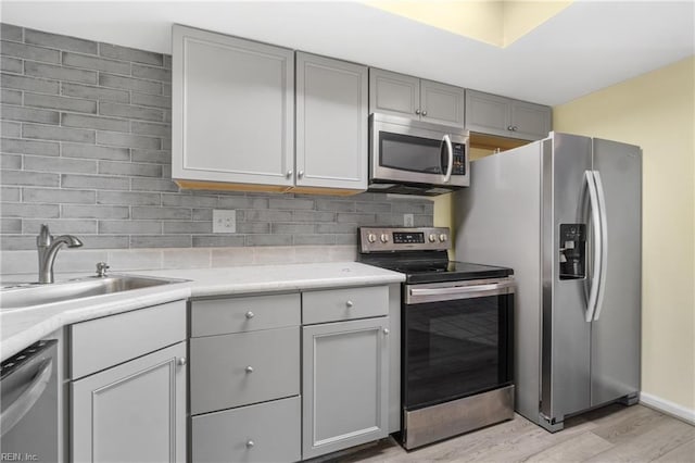 kitchen featuring decorative backsplash, appliances with stainless steel finishes, light countertops, light wood-style floors, and a sink