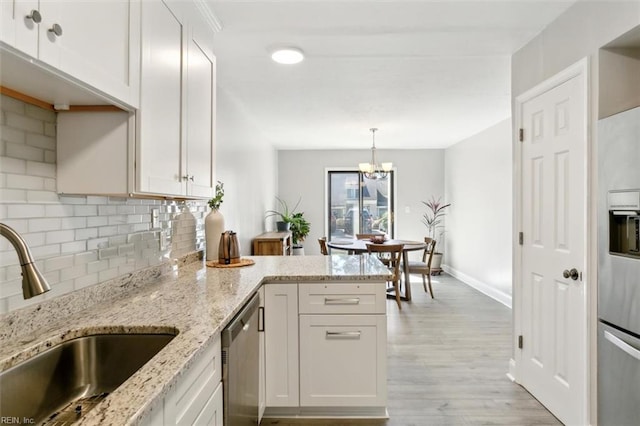 kitchen with light wood finished floors, backsplash, a peninsula, stainless steel dishwasher, and a sink