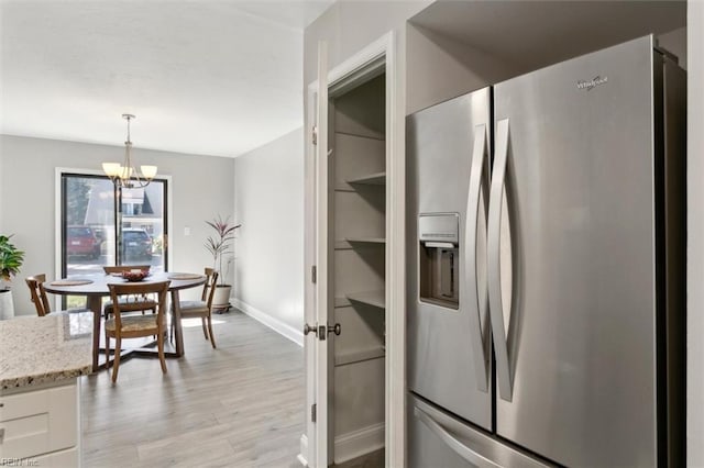 kitchen featuring white cabinets, light wood-style floors, stainless steel fridge with ice dispenser, light stone countertops, and an inviting chandelier