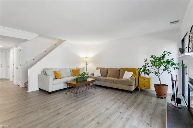 living room featuring a fireplace, light wood finished floors, visible vents, ornamental molding, and stairs