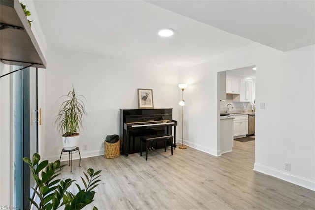 sitting room with baseboards, crown molding, and light wood-style floors