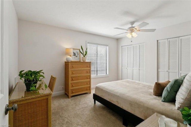 bedroom featuring multiple closets, light colored carpet, ceiling fan, and baseboards