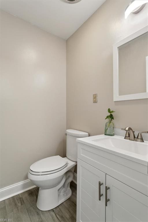 half bath featuring baseboards, vanity, toilet, and wood finished floors