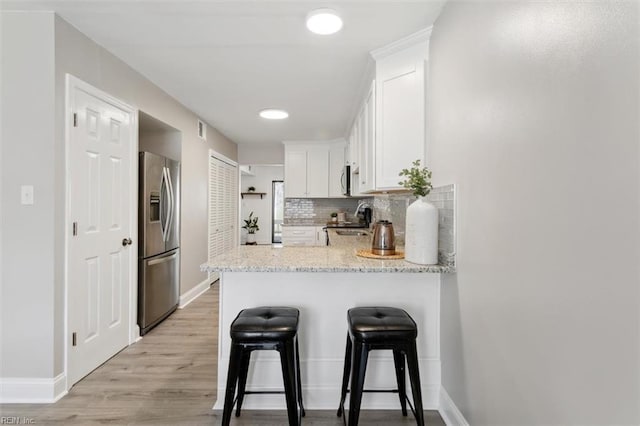 kitchen with a breakfast bar area, tasteful backsplash, appliances with stainless steel finishes, white cabinetry, and a peninsula