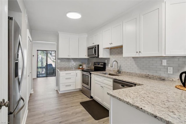 kitchen with appliances with stainless steel finishes, light wood-style flooring, a sink, and light stone counters