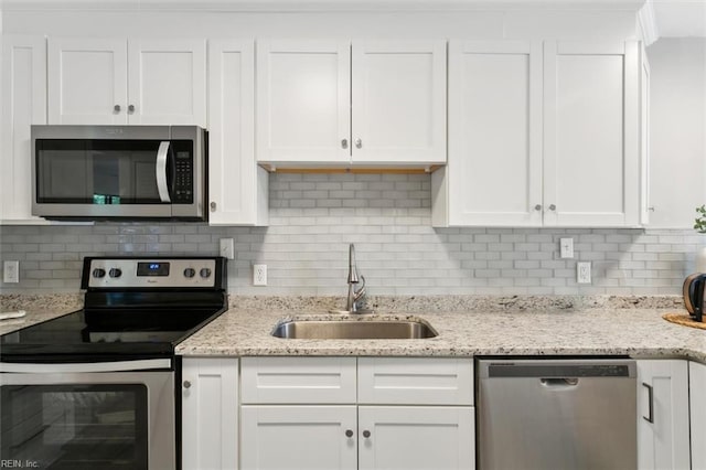 kitchen featuring light stone counters, decorative backsplash, appliances with stainless steel finishes, white cabinets, and a sink