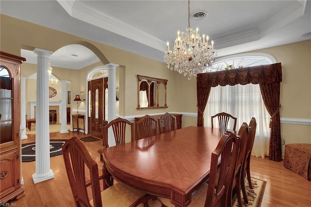 dining area featuring arched walkways, visible vents, light wood-type flooring, and a tray ceiling