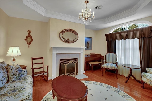 living area with a tray ceiling, visible vents, wood finished floors, and ornamental molding