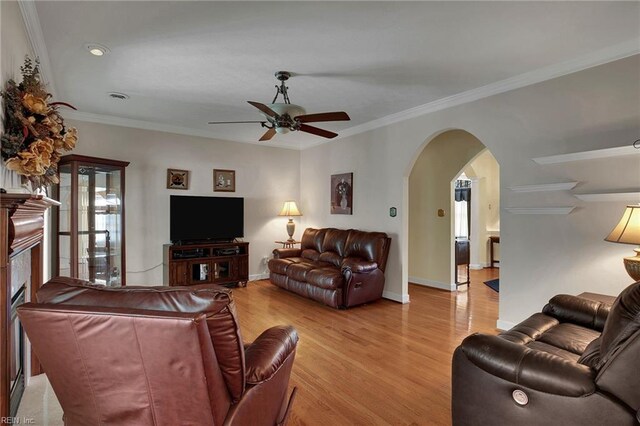 living area featuring baseboards, ceiling fan, ornamental molding, light wood-style floors, and arched walkways