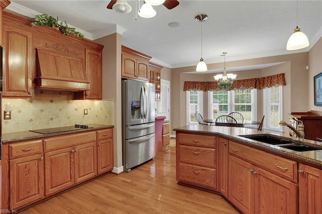 kitchen with black electric stovetop, stainless steel fridge with ice dispenser, custom range hood, ceiling fan with notable chandelier, and a sink