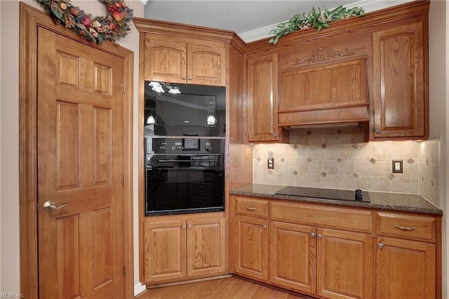 kitchen with dark stone countertops, brown cabinetry, light wood finished floors, black appliances, and backsplash