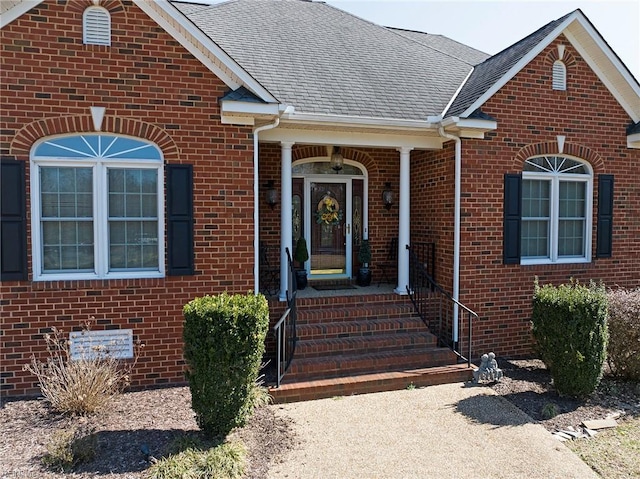 view of exterior entry featuring brick siding and a shingled roof