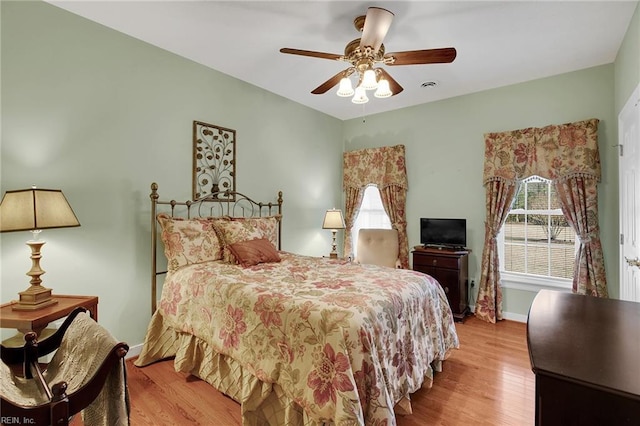 bedroom featuring a ceiling fan, visible vents, wood finished floors, and baseboards