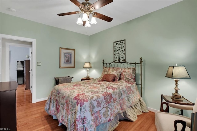 bedroom with wood finished floors, baseboards, freestanding refrigerator, and ceiling fan