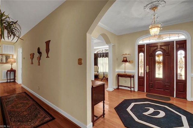 foyer entrance with wood finished floors, visible vents, baseboards, decorative columns, and arched walkways