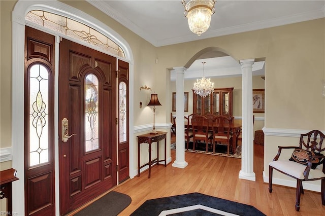 entrance foyer featuring light wood-type flooring, arched walkways, an inviting chandelier, crown molding, and ornate columns