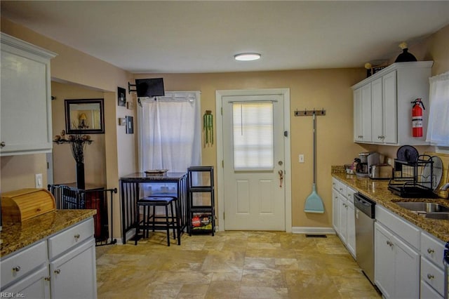 kitchen with stone counters, white cabinets, a sink, dishwasher, and baseboards