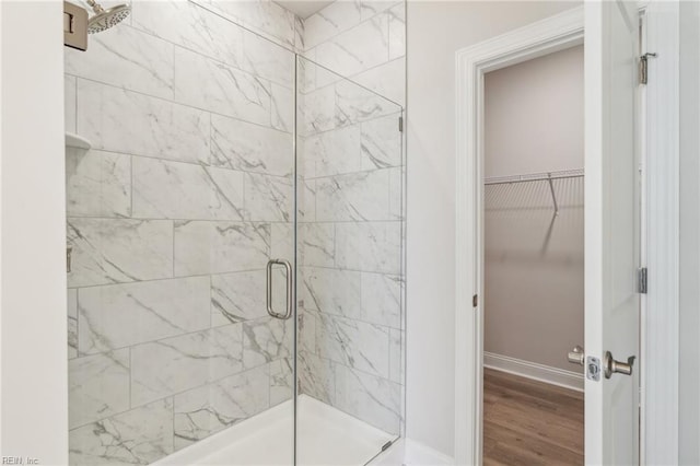 bathroom with a shower stall, a spacious closet, baseboards, and wood finished floors