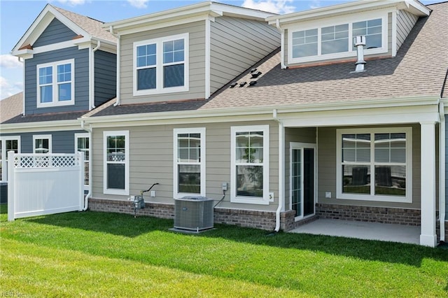 back of property with a shingled roof, fence, central AC unit, and a yard