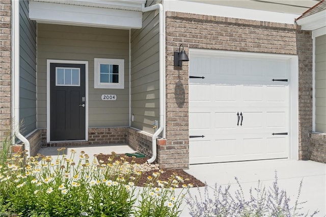 property entrance with a garage, concrete driveway, and brick siding