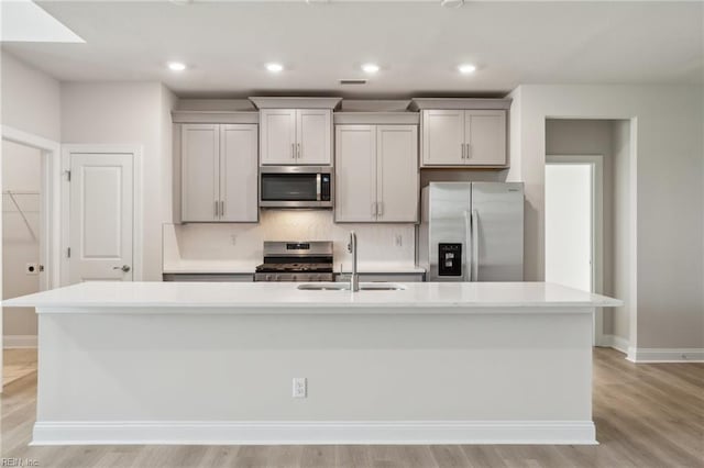 kitchen with a sink, light countertops, appliances with stainless steel finishes, tasteful backsplash, and an island with sink