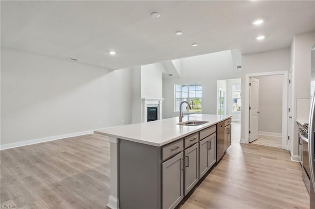 kitchen featuring a fireplace, stainless steel dishwasher, gray cabinetry, open floor plan, and a sink