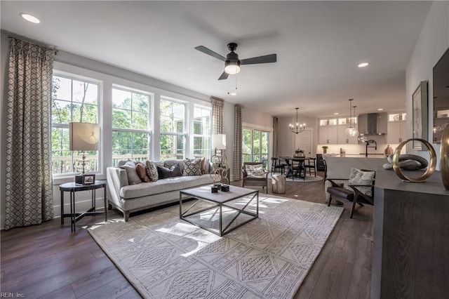living room featuring recessed lighting, ceiling fan with notable chandelier, and dark wood-type flooring