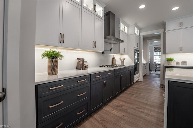 kitchen with light countertops, wall chimney exhaust hood, wood finished floors, stainless steel appliances, and white cabinets