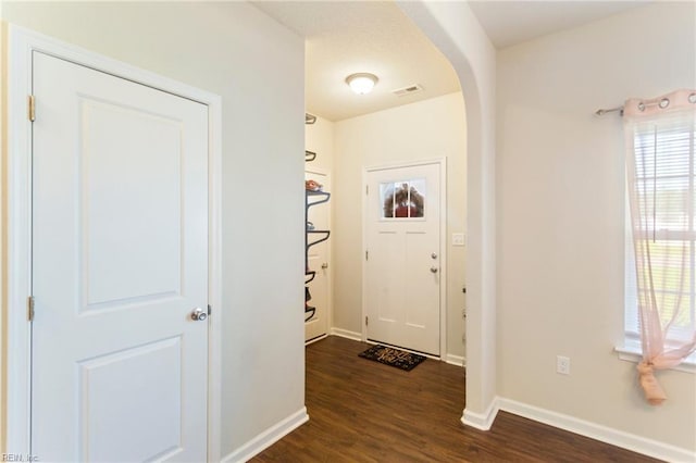 entryway with baseboards, visible vents, arched walkways, and dark wood-type flooring