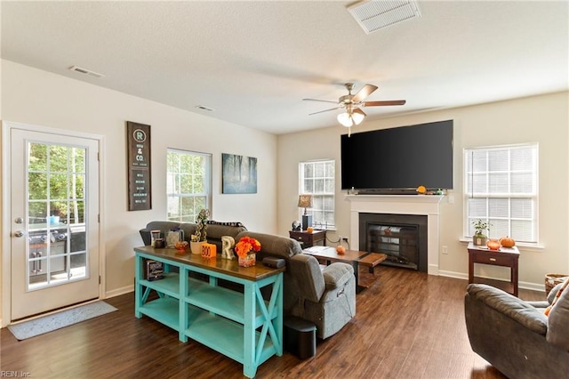 living room featuring dark wood-style floors, a glass covered fireplace, and visible vents