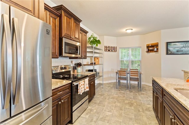 kitchen with appliances with stainless steel finishes, baseboards, light stone counters, and decorative backsplash