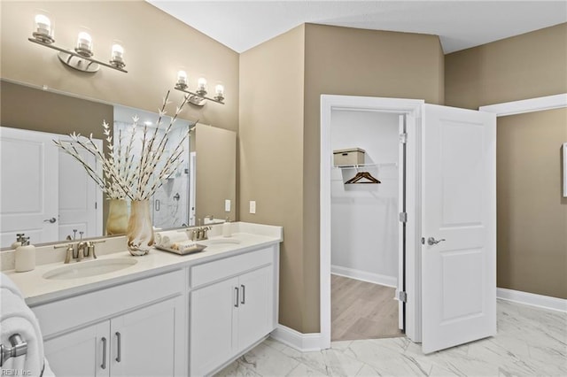 full bathroom featuring marble finish floor, a sink, baseboards, and double vanity