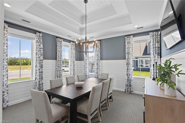 carpeted dining space featuring a wainscoted wall, visible vents, a tray ceiling, and crown molding