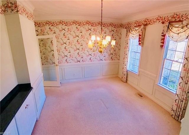 unfurnished dining area featuring wallpapered walls, light colored carpet, a wainscoted wall, a chandelier, and a decorative wall