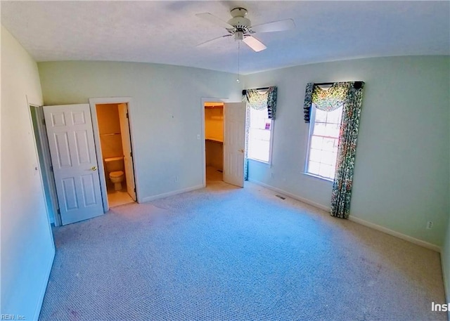 unfurnished bedroom featuring carpet floors, visible vents, baseboards, a walk in closet, and ensuite bath