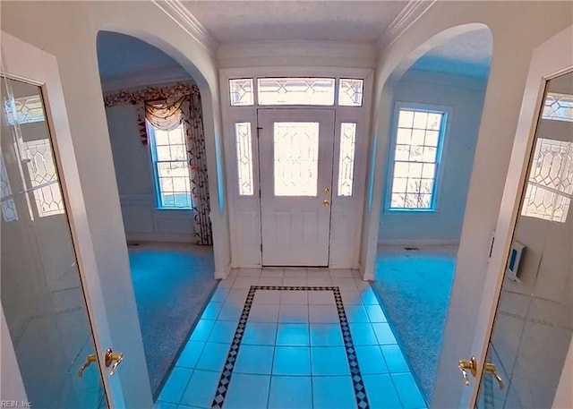 entryway featuring baseboards, arched walkways, tile patterned floors, and crown molding