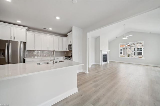 kitchen featuring lofted ceiling, a sink, open floor plan, appliances with stainless steel finishes, and backsplash