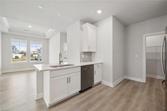 kitchen with a tray ceiling, stainless steel dishwasher, light wood-style floors, white cabinetry, and a sink